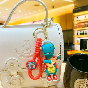 Cute blue dinosaur keychain with guitar and red shoes hanging on white bag