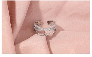 Macro detail of silver adjustable crisscross ring with zircons on pink silk background