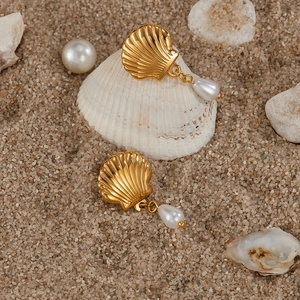 Detailed shot of golden shell earrings with drop pearls on beach sand background