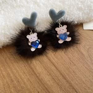 Macro detail of bear pendant with blue heart gemstone and plush pompom earring