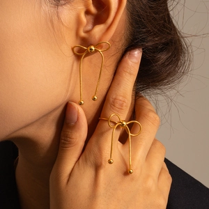 Close-up of golden woven bow tie earrings and matching ring on model with soft lighting
