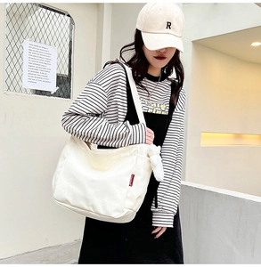 Close-up of minimalist cream canvas shoulder bag with plush charm on a model outdoors