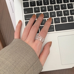 Close-up of a 925 silver hollow letter B ring worn on the index finger over a laptop
