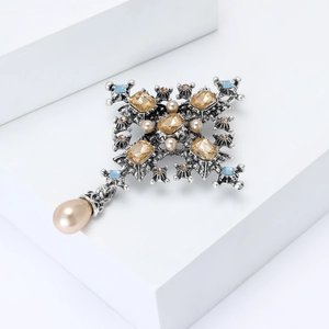 Close-up of Baroque silver cross brooch with gold crystals and hanging pearl pendant