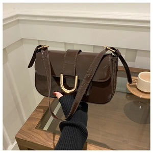 Detailed shot of dark brown glossy patent leather shoulder bag with gold U-shaped buckle