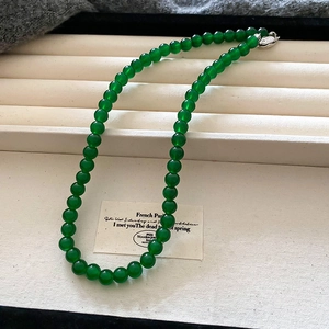 Close-up of green beaded pearl necklace with silver clasp on white jewelry tray