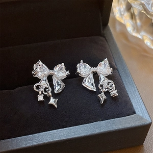 Detailed macro view of silver bow-shaped earrings with heart-cut zircons and star drops