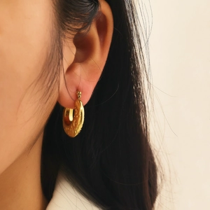 Detail of golden hoop earring with hammered texture on a model showing actual size