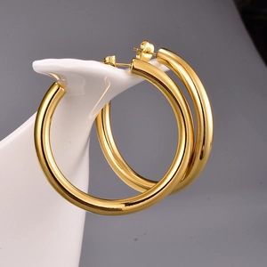 Close-up of thick golden hoop earrings with polished mirror finish on white ceramic stand