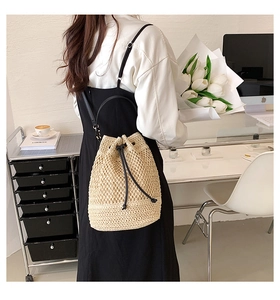 Detail of beige woven straw bucket bag with black leather drawstring on a model
