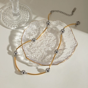 Minimalist gold and silver two-tone curved tube bead necklace on a decorative glass dish