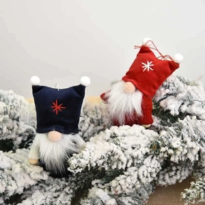 Christmas faceless gnome ornaments in red and navy knit on snow-covered pine branches