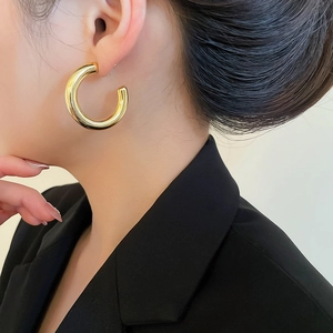Close-up of a large gold polished C-shaped chunky hoop earring worn by a model