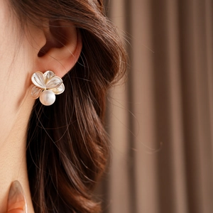 Gros plan d'une boucle d'oreille fleur plaquée or avec nacre et une perle blanche pendante