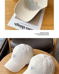 Detail of white cotton baseball cap with blue heart embroidery on a rustic wooden table