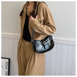 Detail of black glossy patent leather moon bag with rivets and straps worn by a model