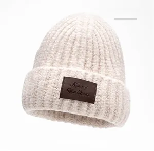 Detailed close-up of beige knit beanie showing vertical ribbed texture and leather tag