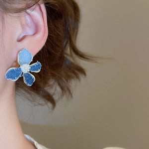 Close-up of blue denim flower C-shape earring with a white pearl center on model