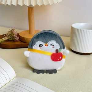 Detailed view of gray penguin plush coin purse with red apple strap in a warm home setting