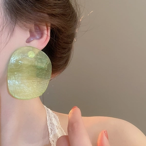 Close-up of translucent light green resin hoop earrings with elegant ripple texture