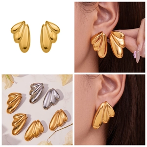 Polished angel wing earrings in gold and silver finish shown on ears and marble
