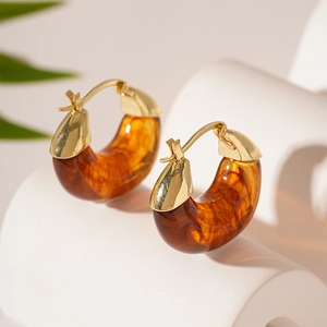 Detail view of amber resin and gold U-shaped hoop earrings on a minimalist white pedestal