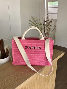 Close-up of pink woven tote bag with white long straps and PARIS embroidery on light wood