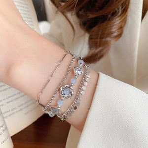 Detail of layered silver bracelets featuring paperclip chains and blue bead accents on wrist