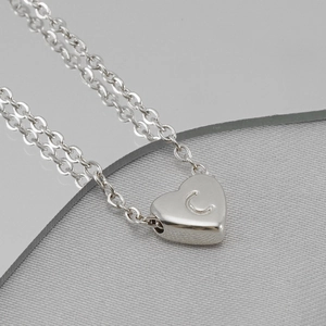 Gros plan d'un pendentif cœur argenté avec la lettre C sur un collier en acier inoxydable