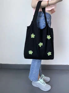 Detail of 3D embroidered flowers on a black canvas tote bag worn on shoulder
