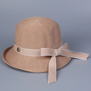 Detail of knitted bucket hat with ribbon bow and floral metal button on a beige texture