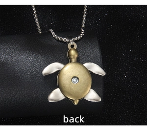 Detail of a turtle pendant in gold and silver finish resting on a textured black stand