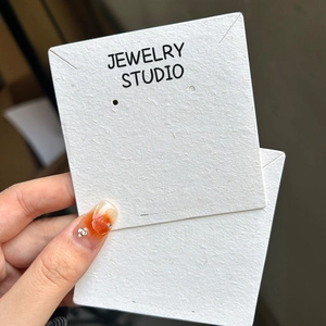 Close-up of premium white textured paper jewelry display cards with gold studio logo