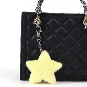 Detail of yellow plush star charm on a black quilted leather handbag with striped handle