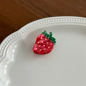 Detail view of cute red strawberry hair claw clip with white dots and green leaves