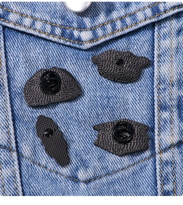 Detail view of cartoon enamel pin backs with metal butterfly and rubber clutches on denim