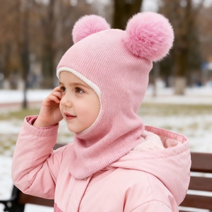Close-up of pink knitted baby balaclava with two large pompoms for winter warmth