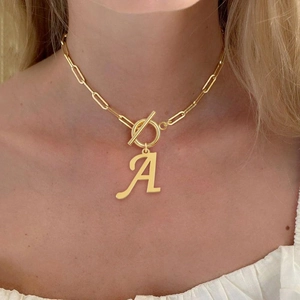 Close-up of gold paperclip chain necklace with T-bar clasp and letter A pendant on model