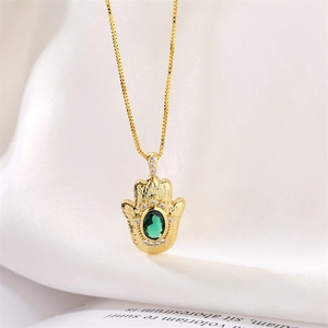 Detail of Hamsa Hand pendant with green gemstone on a golden chain and silk fabric