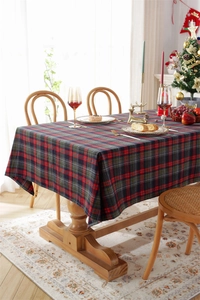 Detail of red and green plaid Christmas tablecloth with natural drape on a wooden table