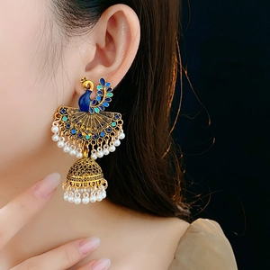 Detailed view of peacock jhumka earring with blue enamel and white pearls on model