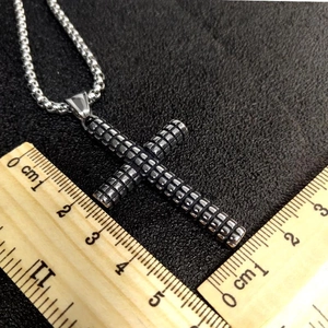 Detailed measurement of stainless steel cross pendant with checkered texture on ruler