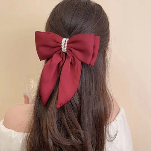 Detail of burgundy satin bow hair clip with pearl beads on an elegant half-up hairstyle