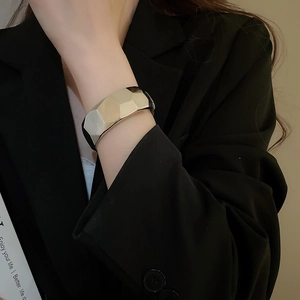Detailed close-up of glossy irregular geometric metal bracelet on a black blazer sleeve