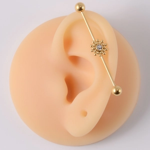 Detailed shot of golden stainless steel industrial barbell with flower gemstone on ear
