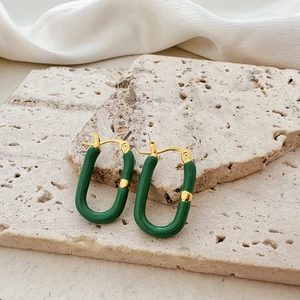 Detail of U-shaped gold earrings featuring dark green enamel on textured stone surface