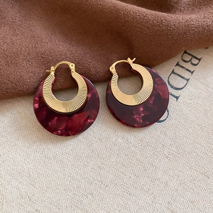 Close-up of retro gold metal hoop earrings with dark red marble texture resin charms