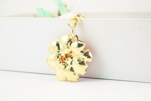 Detailed view of a golden flower-shaped metal pendant with a secure metal clasp buckle