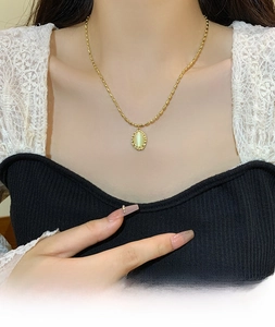 Close-up of elegant gold bead chain necklace with oval opal pendant worn by a model