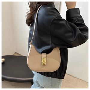 Détail du sac hobo croissant beige avec boucle dorée porté sur une veste en cuir noir
